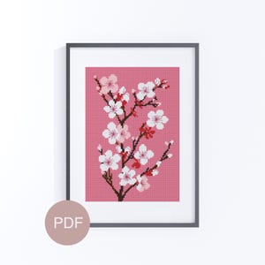 Könnte beinhalten: Gerahmtes Kreuzstich-Kunstwerk mit einem Kirschblütenzweig mit weißen und rosa Blüten vor einem rosa Hintergrund. Das Kunstwerk befindet sich in einem schwarzen Rahmen und enthält ein PDF-Symbol.