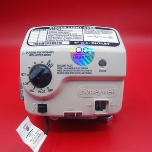 May include: A white Honeywell gas valve with a black knob and a status light code chart. The valve has a 4" w.c. outlet and a QC passed sticker. The valve is connected to a white wire.