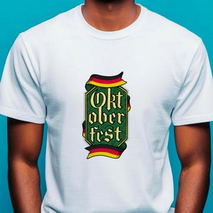 May include: White t-shirt featuring a green and gold Oktoberfest design. The design includes the text "Oktoberfest" in a stylized font, framed by a ribbon in the colors of the German flag. The shirt is made of a soft material.