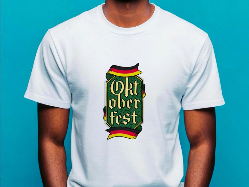 May include: White t-shirt featuring a green and gold Oktoberfest design. The design includes the text "Oktoberfest" in a stylized font, framed by a ribbon in the colors of the German flag. The shirt is made of a soft material.