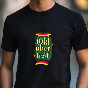 May include: Black t-shirt with a colorful Oktoberfest design. The graphic features the words "Oktoberfest" in a decorative font, framed by a green and yellow border with red and black accents. The shirt is made of a soft material.