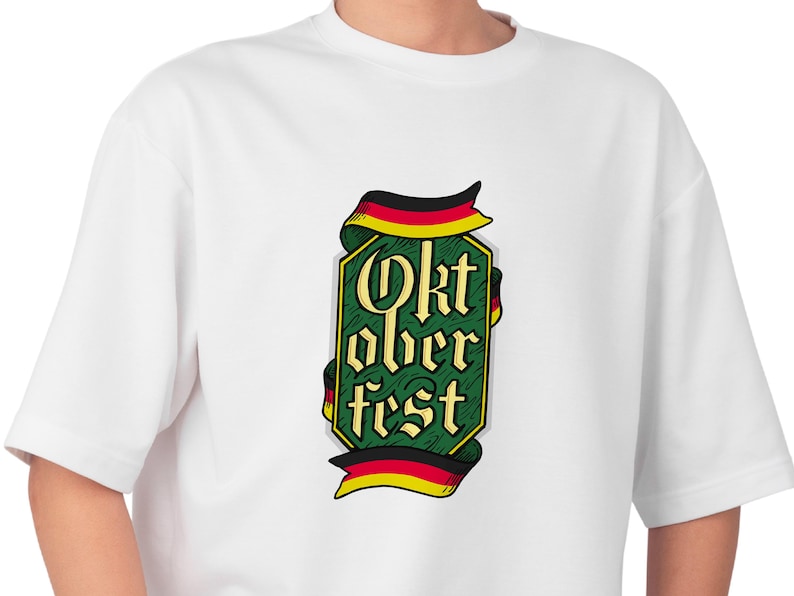 May include: White t-shirt featuring a green and gold Oktoberfest design with the text "Oktoberfest" in a stylized font. The design includes ribbons in the colors of the German flag. A casual, comfortable tee.