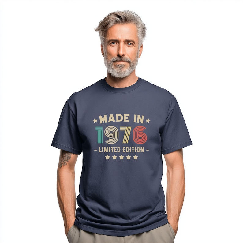 May include: Navy blue t-shirt featuring the text "MADE IN 1976 - LIMITED EDITION" in a retro style. The text is in teal, red, and beige. The shirt has a crew neck and short sleeves, suitable for casual wear.