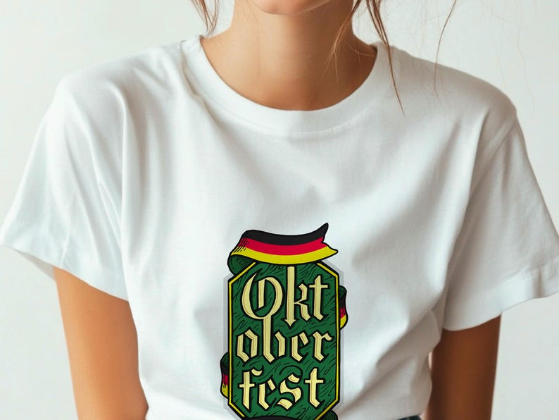 May include: White t-shirt featuring a green and gold Oktoberfest design. The design includes the words "Oktoberfest" in a stylized font, with a ribbon in the colors of the German flag.