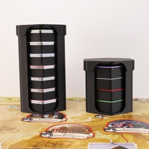 May include: A set of three ceramic mugs with a speckled, matte finish. The mugs are in shades of cream, light gray, and dark gray. Each mug has a simple, minimalist design and a rounded handle. The mugs are likely for coffee or tea.
