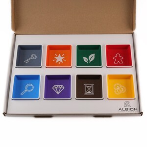 May include: A set of eight square, colourful plastic component trays arranged in a cardboard box. Each tray features a unique white icon, including a key, star, leaves, meeple, magnifying glass, diamond, hourglass, and coins. The box displays the Albion logo.