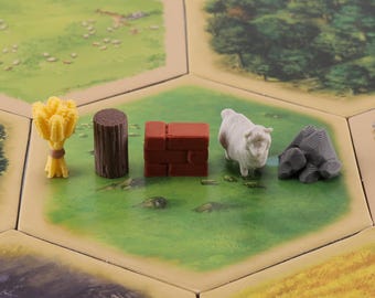 以下が含まれることがあります： さまざまな資源トークンを備えたボードゲームのクローズアップ。トークンには、小麦の束、丸太、レンガ構造、羊、岩の山が含まれます。ゲームボードは六角形のタイルデザインです。