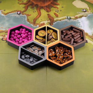 May include: Six hexagonal game pieces with different colored lids and compartments. The lids are pink, yellow, orange, brown, and gray. The compartments contain small game pieces, including wooden tokens, plastic gems, and small wooden sticks.