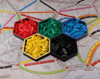 以下が含まれることがあります： アメリカとカナダの地図が描かれたボードゲーム。赤、緑、青、黄、黒のプラスチック製の列車車両が入った6つの六角形の容器。ゲーム盤にはヘレナ、サンタフェ、ダルースなどの都市名が表示されています。