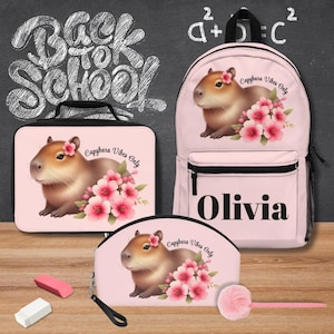 May include: A pink backpack, lunch bag, and pencil case set. Each item features a capybara illustration with pink flowers and the text "Capybara Vibes Only." The backpack has the name "Olivia" printed on it.