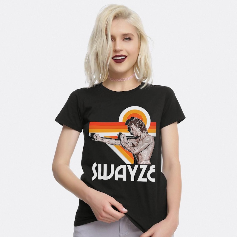 May include: Black t-shirt with a retro-style graphic of Patrick Swayze in a karate pose. The graphic features orange, red, and yellow stripes and the text "SWAYZE".