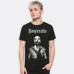 May include: Black t-shirt with the word "Nosferatu" in white gothic lettering. Below the text is a black and white portrait of a woman wearing a patterned top.