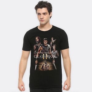 May include: Black t-shirt featuring a graphic print of the film Gladiator II. The print depicts various characters from the movie, including the title "Gladiator II" in gold lettering.