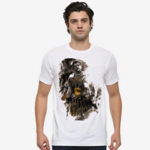 May include: White t-shirt with a black and gold illustration of a historical figure. The graphic shows a man in armour with a detailed design. The shirt has a classic crew neck.