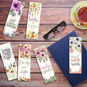 May include: A collection of floral watercolor bookmarks with various quotes. The bookmarks feature phrases like "Just one more chapter," "Books & Coffee," and "Reading Goals." The designs include flowers in shades of purple, pink, and orange.