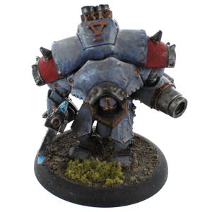 May include: A blue and red painted metal robot miniature with a large cannon on its right arm and a smaller weapon on its left arm. The robot is standing on a black base with green moss.