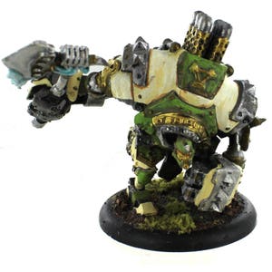 May include: A green and white painted miniature wargaming figure of a robot with a large axe, standing on a black base.
