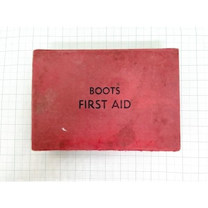 May include: A red Boots First Aid kit with the words "BOOTS FIRST AID" printed in white. The kit is rectangular and shows signs of wear. The background is a white grid pattern. The text is centered on the front.