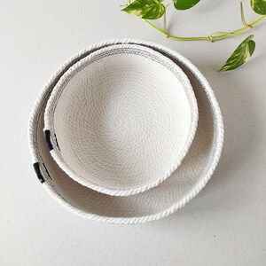 May include: Two white rope bowls with black trim, the smaller bowl is nested inside the larger bowl.