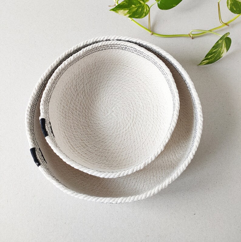 May include: Two white rope bowls with black trim, the smaller bowl is nested inside the larger bowl.