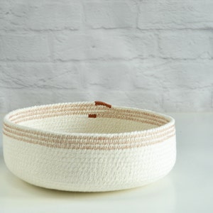 May include: A white woven basket with brown trim. The basket is round and has a wide opening.