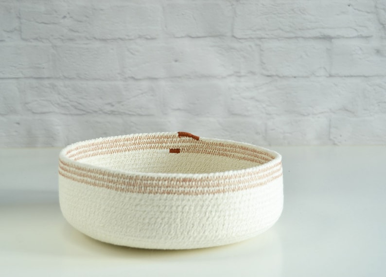 May include: A white woven basket with brown trim. The basket is round and has a wide opening.