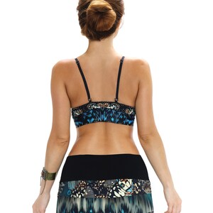 May include: A blue and black patterned crop top and skirt set. The top has thin black straps and a butterfly-like design. The skirt features a layered design with a mix of blue, black, and white butterfly patterns. The model is facing away from the camera.