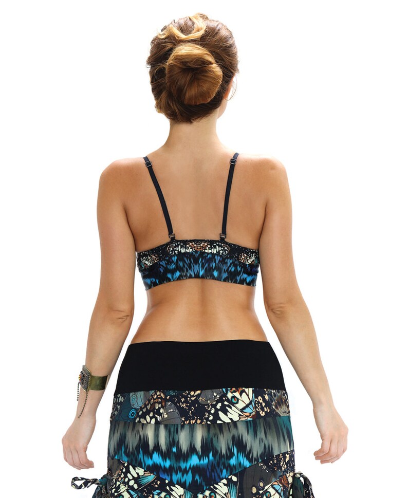 May include: A blue and black patterned crop top and skirt set. The top has thin black straps and a butterfly-like design. The skirt features a layered design with a mix of blue, black, and white butterfly patterns. The model is facing away from the camera.