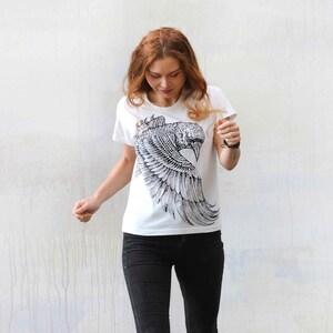 Puede incluir: Una camiseta blanca con un estampado gr&aacute;fico en blanco y negro de un p&aacute;jaro con las alas extendidas.