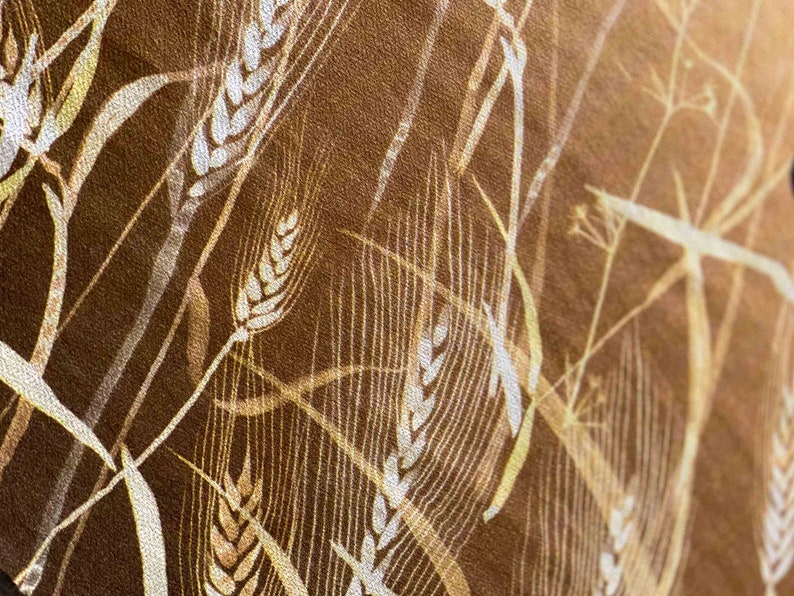 May include: A close-up of a brown fabric with a white wheat pattern. The fabric has a textured surface and a subtle sheen.