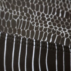 May include: Close-up of black fabric with a white snake skin pattern and a white striped pattern. The fabric has a seam running horizontally across the middle.