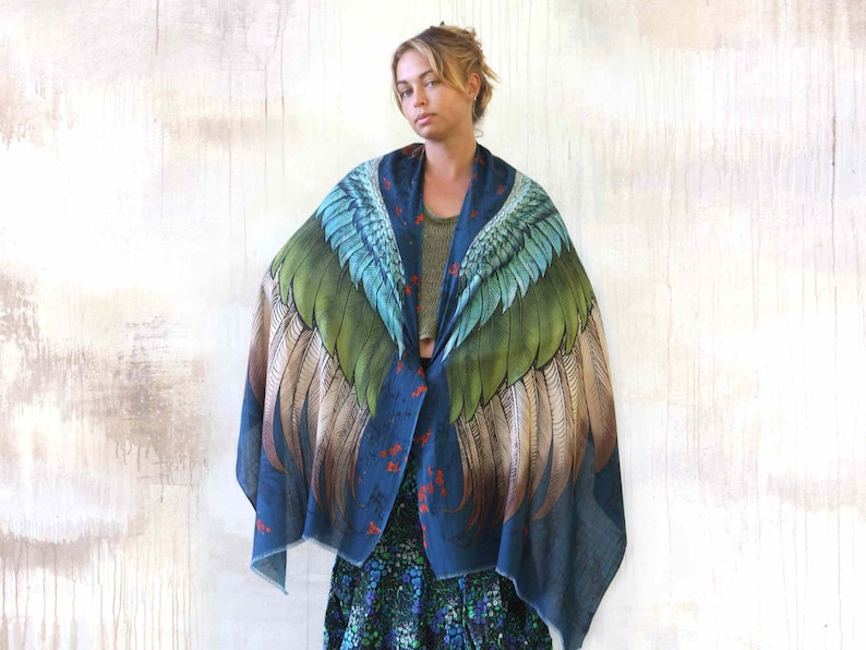 Puede incluir: Un chal azul oscuro con un gran dise&ntilde;o de alas en tonos verdes, azules y marrones. Las alas est&aacute;n extendidas, creando un efecto dram&aacute;tico. El chal tiene un estampado floral y detalles rojos.
