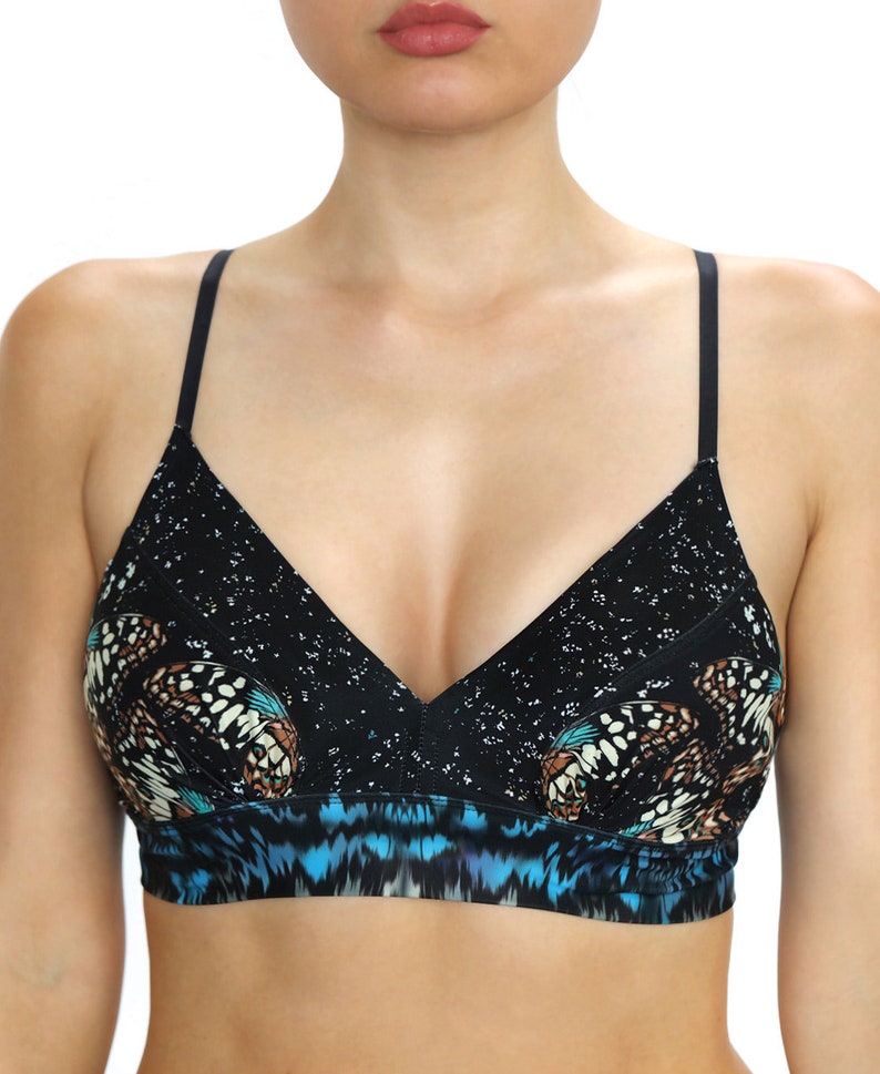 May include: A black bralette with a butterfly print. The bralette features a V-neck design with thin black straps. The top portion has a speckled pattern, while the lower section showcases a blue and black design.