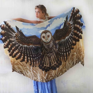 May include: A white silk scarf with a brown and white owl design. The owl has its wings spread wide and is surrounded by a blue sky and brown grass.