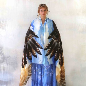 May include: A blue and brown silk scarf with a bird wing design. The scarf is draped over a person's shoulders and the wings are spread out.