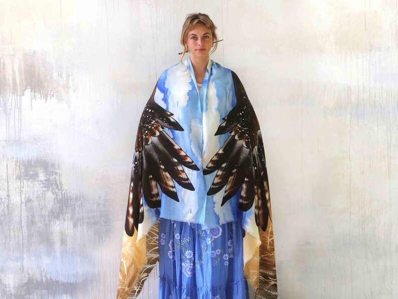 May include: A blue and brown silk scarf with a bird wing design. The scarf is draped over a person's shoulders and the wings are spread out.