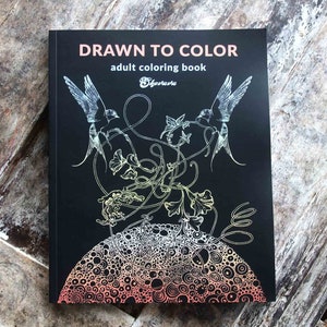 K&ouml;nnte beinhalten: Ein Schwarzwei&szlig;-Malbuchcover mit dem Titel "Drawn to Color" und dem Untertitel "Malbuch f&uuml;r Erwachsene". Das Cover zeigt eine detaillierte Illustration von zwei V&ouml;geln, die &uuml;ber einem wirbelnden Ranken mit einem kreisf&ouml;rmigen Muster im Hintergrund fliegen.