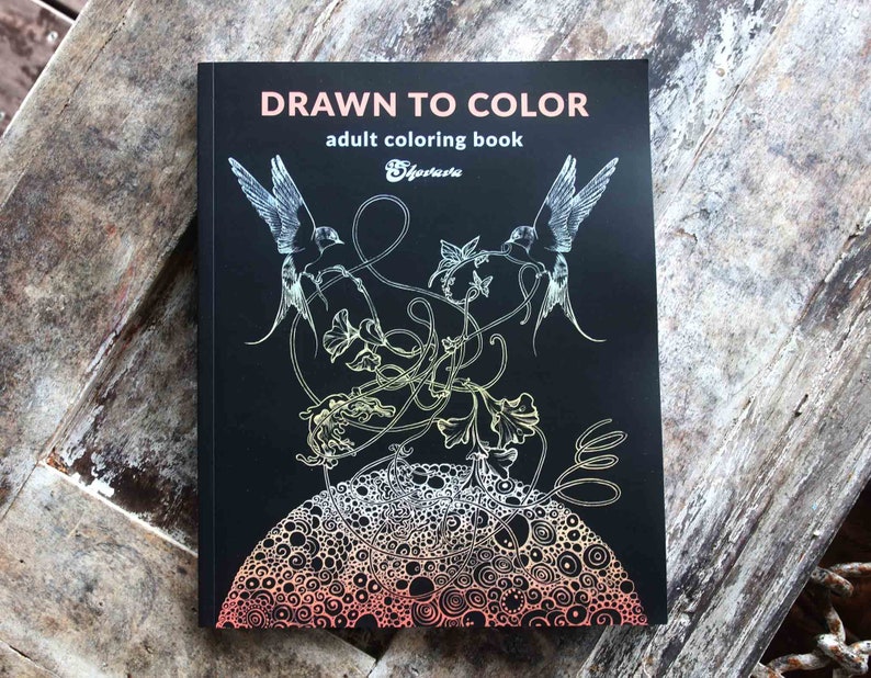 K&ouml;nnte beinhalten: Ein Schwarzwei&szlig;-Malbuchcover mit dem Titel "Drawn to Color" und dem Untertitel "Malbuch f&uuml;r Erwachsene". Das Cover zeigt eine detaillierte Illustration von zwei V&ouml;geln, die &uuml;ber einem wirbelnden Ranken mit einem kreisf&ouml;rmigen Muster im Hintergrund fliegen.