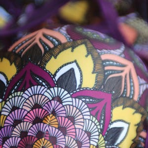 May include: Purple and yellow fabric with a mandala pattern. The pattern features intricate details in shades of pink, orange, and white.