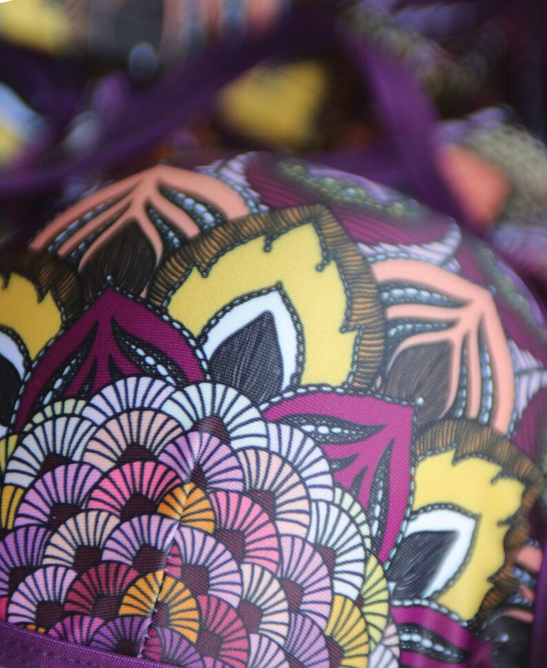 May include: Purple and yellow fabric with a mandala pattern. The pattern features intricate details in shades of pink, orange, and white.