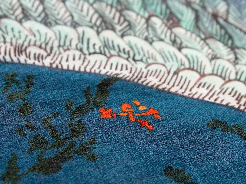 Puede incluir: Primer plano de un textil color turquesa con un dise&ntilde;o floral. La tela presenta ramas de color verde oscuro y peque&ntilde;as flores naranjas. La parte superior de la imagen muestra un patr&oacute;n blanco y azul claro, posiblemente un dise&ntilde;o de olas o plumas.