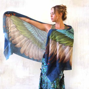 Puede incluir: Una bufanda rectangular grande con un dise&ntilde;o detallado de alas. La bufanda presenta un degradado de colores, incluyendo azul, verde y marr&oacute;n, con un patr&oacute;n de plumas. La bufanda se sostiene, mostrando el dise&ntilde;o completo.