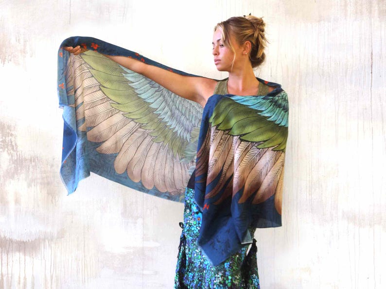 Puede incluir: Una bufanda rectangular grande con un dise&ntilde;o detallado de alas. La bufanda presenta un degradado de colores, incluyendo azul, verde y marr&oacute;n, con un patr&oacute;n de plumas. La bufanda se sostiene, mostrando el dise&ntilde;o completo.