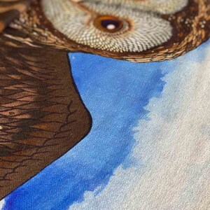 May include: A close-up of a brown and white owl with a blue and white background. The owl's feathers are detailed and the background is a watercolor wash.