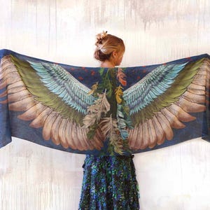Puede incluir: Bufanda azul oscuro con un dise&ntilde;o detallado de alas de p&aacute;jaro en tonos verdes, azules y marrones. La bufanda est&aacute; drapeada, mostrando el patr&oacute;n de las alas. Tambi&eacute;n se ven plumas y follaje.