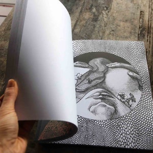 K&ouml;nnte beinhalten: Eine Schwarzwei&szlig;illustration einer Schlange, die sich um eine Hand mit Blumen windet. Die Illustration befindet sich auf einer Buchseite mit einem schwarz-wei&szlig;en Muster im Hintergrund.