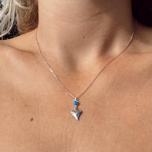 May include: A silver necklace featuring a blue gemstone and a shark tooth pendant.