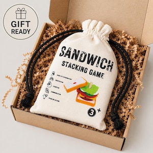 Pu&ograve; includere: Una borsa in tela color crema con coulisse che riporta il testo nero SANDWICH STACKING GAME, un'illustrazione di un panino in legno, cinque piccole icone con etichette e un'indicazione di et&agrave; 3+, all'interno di una scatola con carta di riempimento.