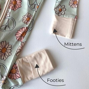 May include: A light green baby sleeper with a daisy and peace sign pattern. The sleeper has beige cuffs and footies. The image shows the details of the mittens and footies.