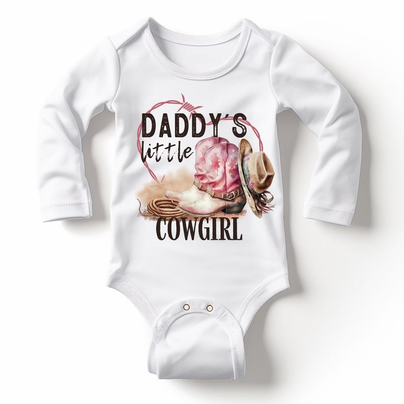K&ouml;nnte beinhalten: Wei&szlig;er Baby-Body mit langen &Auml;rmeln. Der Body zeigt eine Grafik eines rosa Cowboy-Stiefels, eines braunen Cowboyhuts und den Text "DADDY'S little COWGIRL" in Schwarz. Ein herzf&ouml;rmiges Stacheldrahtdesign in Rot umgibt die Grafik.